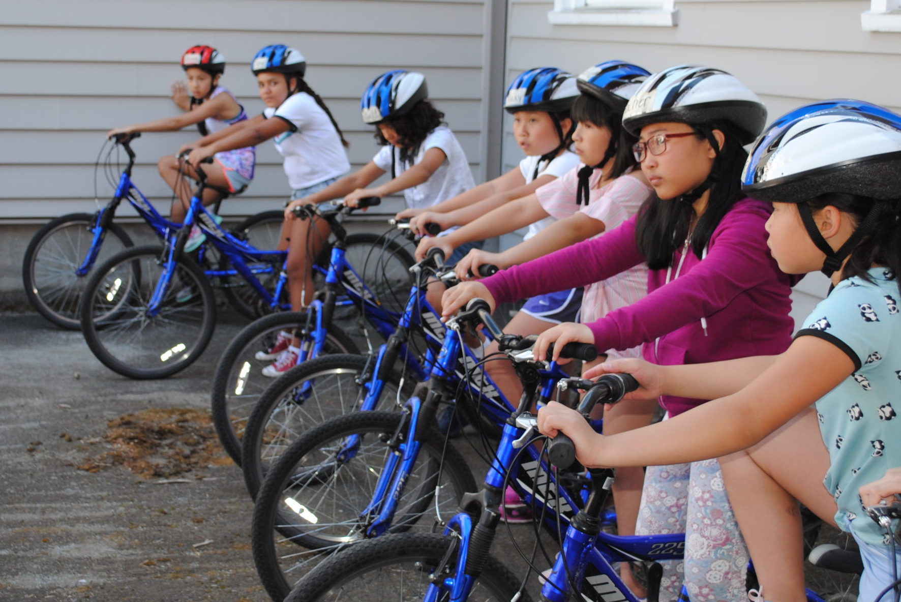 A group of children wearing helmets sit on bikes in a row.