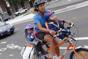 A mother on a bike has two children also on the bike with her.
